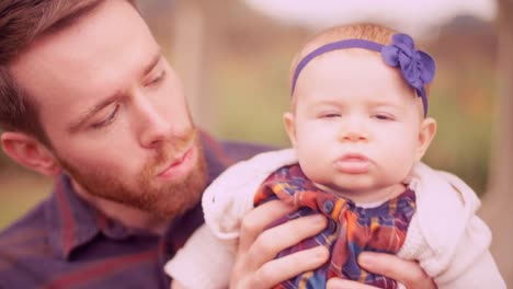 A-young-man-playing-with-his-baby-daughter-under-a-gazebo,-and-giving-her-a-kiss-on-the-cheek,-close-up