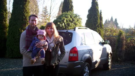 Portrait-of-a-young-mother,-father-and-baby-in-front-of-their-car-with-Christmas-tree-on-top