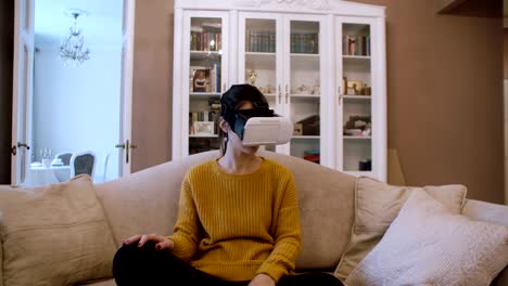 Schöne-junge-Frau-sitzt-auf-dem-Sofa-im-Wohnzimmer-und-VR-Kopfhörer-verwenden.-4K