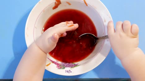 An-attractive-boy-2-years-old-is-eating-red-soup-himself.-He-climbs-his-hands-in-the-plate.-Table-top-view