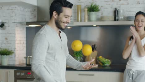 El-joven-animado-impresiona-a-su-novia-haciendo-malabares-con-naranjas-en-la-cocina.