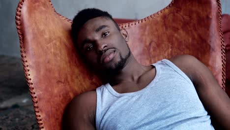 Portrait-of-young-handsome-african-man-sitting-on-the-leather-chair-and-looking-at-camera.-Serious-model-male