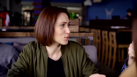 Close-up-of-a-young-beautiful-woman-sitting-at-the-restaurant-and-spending-time-in-the-society-of-her-friends.-Adorable-lady-in-green-blouse-speaking-and-looking-at-her-company