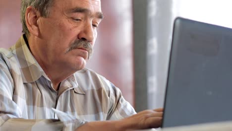 An-elderly-man-with-a-mustache-sits-behind-a-laptop-and-solves-problems.-He-looks-seriously-at-the-monitor