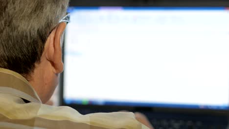 An-elderly-man-with-a-mustache-sits-behind-a-laptop-and-solves-problems.-He-looks-seriously-at-the-monitor