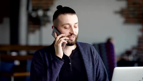 Ein-erwachsener-Mann-mit-einem-Bart-im-Gesicht,-legte-seine-Haare-des-Schwanzes-auf-seinem-Handy-mit-einem-Geschäftspartner-in-einem-Restaurant-zu-sprechen,-bis-er-gebracht-wurde-Abendessen