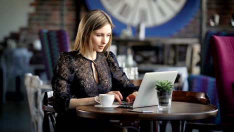 Schöne-Frau-im-schwarzen-sexy-Kleid-sitzt-am-Tisch-im-Restaurant-mit-modernen-Laptop.-Berühmte-Schönheit-Blogger-arbeiten-im-mobilen-Büro-in-den-Coffee-Shop-Chat-mit-Anhänger-auf-digitalen-Gerät