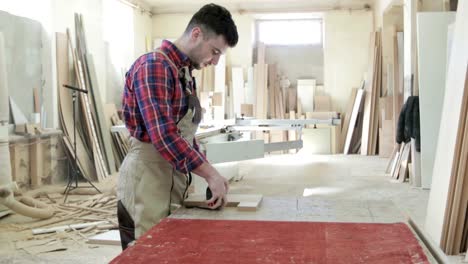 4K-A-young-man-works-on-furniture-production.-Carpenter-or-joiner-worker`s-hands-using-roulette,-measuring-something-on-wooden-plank.