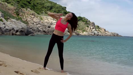 Healthy-sporty-woman-exercising-and-stretching-back-for-warming-up-before-running-on-beach-near-sea.-Female-doing-side-incline-body-exercise.