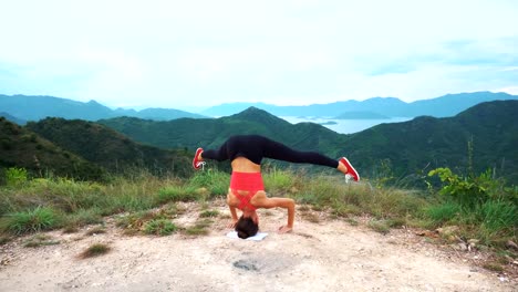 Junge-Frau-praktizieren-Yoga-Kopfstand-auf-Felsen.-Blick-auf-die-Berge-Landschaft.