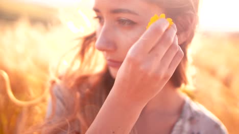 Young-woman-with-yellow-flower-standing-in-a-golden-field