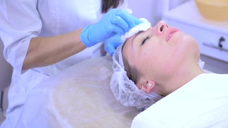 Beautician-cleans-female's-face-skin-in-beauty-clinic