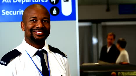 Smiling-security-staff-holding-metal-detector-standing-at-airport