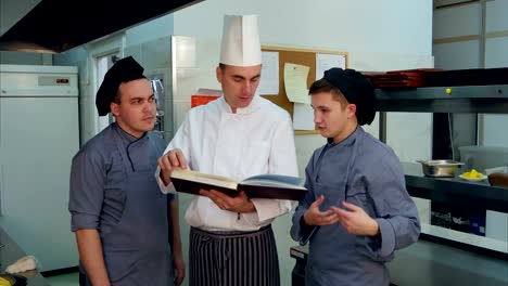 Head-chef-holding-recipe-book-and-discussing-something-with-his-trainees