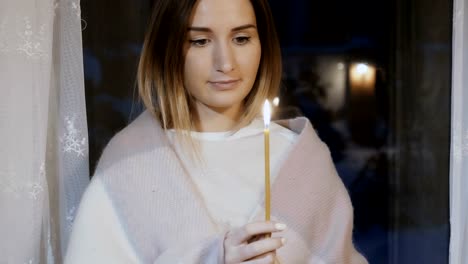 Hermosa-chica-en-tela-escocesa-con-la-grabación-de-velas-contra-la-ventana-de-noche