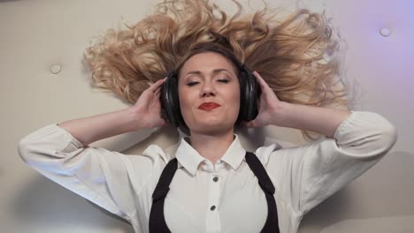 Woman-lying-on-the-bed,-listens-to-music-in-big-headphones-and-reacts-to-her-sexually-smiling-middle-frame