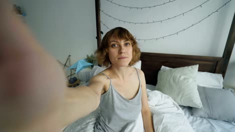 Junge-fröhliche-Frau,-die-unter-Selfie-Porträt-mit-Smartphone-sitzen-im-Bett-zu-Hause