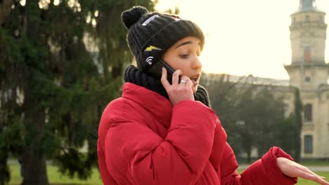 Charming-student-in-warm-clothes-talks-on-phone-near-campus