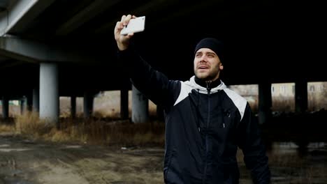 Hombre-deportivo-feliz-tomando-selfie-retrato-con-smartphone-después-de-entrenar-en-lugar-urbano-al-aire-libre-en-invierno