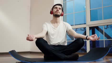 Chico-joven-meditando-sobre-el-piso-y-escuchar-música-en-auriculares