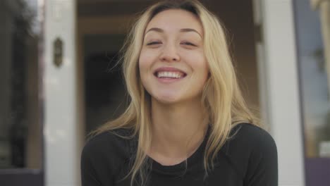 Portrait-shot-of-a-beautiful-Asian-woman-sitting-on-her-porch,-and-smiling-at-the-camera