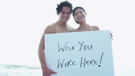 Happy-Ethnic-couple-displaying-vacation-greetings-white-board