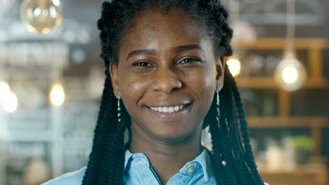 Portrait-of-a-Beautiful-African-American-Cafe-Owner-Walking-into-Focus-while-in-the-Background-Her-Stylish-Coffee-House-Shines-with-Lights.