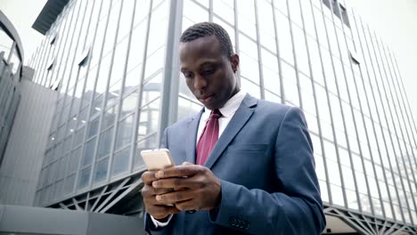 young-afro-american-businessman-in-the-street-types-on-his-smartphone