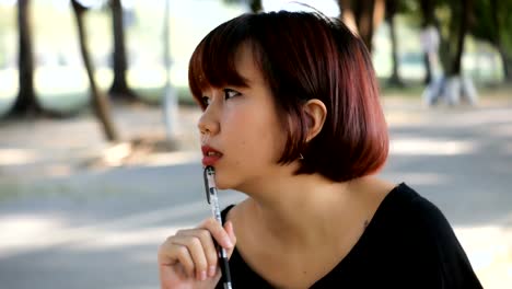 Happy-hipster-young-asian-woman-writing-into-her-diary-in-park.-Happy-hipster-young-asian-woman-working-on-notebook-in-park.-Student-studying-outdoors.-Lifestyle-woman-outdoor-concept.