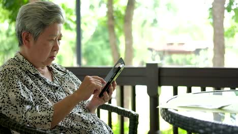 Asia-mujer-mayor-sosteniendo-el-teléfono-móvil-mientras-está-sentado-en-la-silla-en-el-restaurante.-mensaje-de-texto-mujeres-mayores,-con-la-aplicación-de-teléfono-móvil-en-el-parque.-smartphone-de-mayor-uso-para-conectar-con-la-gente-en-red-social-con-exterior-de-conexión-de-internet-inalámbrica.