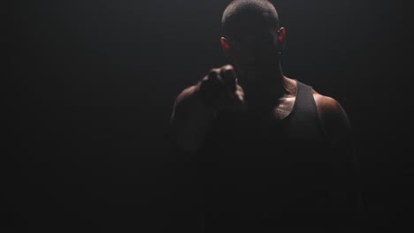 Portrait-shot-of-a-muscular-black-man-pointing-at-the-camera-on-a-dark-background.
