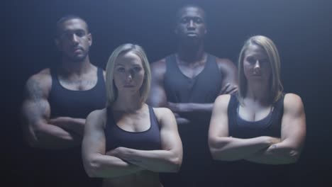 Group-of-athletes-staring-at-the-camera-with-their-arms-crossed-on-a-foggy-dark-background