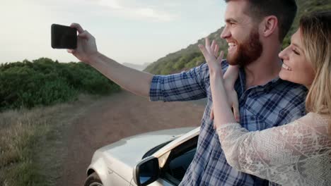 Couple-on-road-trip-taking-selfies-by-convertible