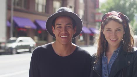 A-young-couple-standing-together-on-a-city-street-and-smiling,-portrait