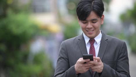 Young-handsome-Asian-businessman-using-phone-in-the-streets-outdoors