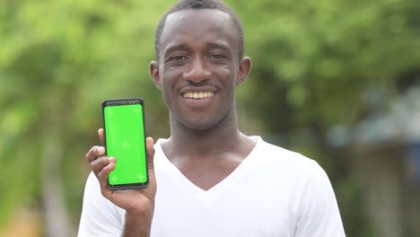 Young-happy-African-man-smiling-while-showing-phone-in-the-streets-outdoors