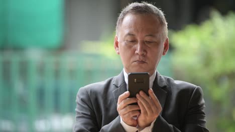 Mature-Japanese-businessman-using-phone-in-the-streets-outdoors