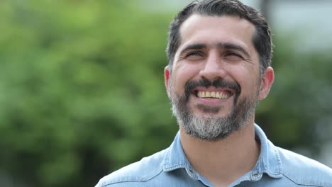 Happy-Persian-bearded-man-smiling-while-thinking-in-the-streets-outdoors