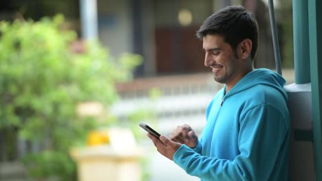 Glücklich-persischer-Jüngling-mit-Telefon-im-freien