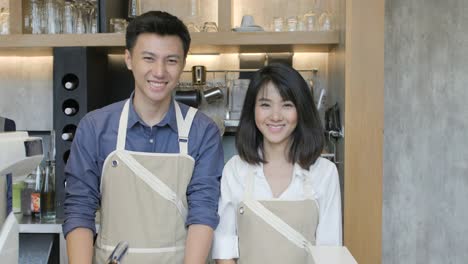 Retrato-de-dos-jóvenes-asiáticos-barista-hombre-y-mujer-cruzando-las-manos-y-sonriendo-a-la-cámara-en-la-cafetería-de-café