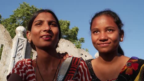 Two-women-bonding-talking-sharing-sitting-staring-in-same-place-side-profile-on-a-terrace-in-traditional-dress-in-India-handheld--two-medium-shot-love-tradition-rural-outdoor-summer-heat-sun