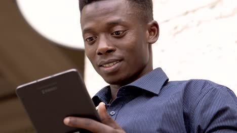 Smiling-black-american-student-using-tablet-in-the-street