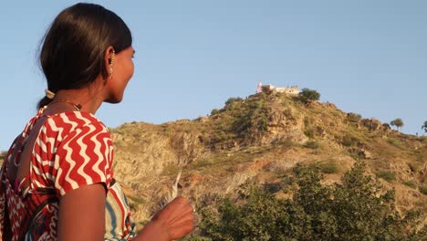 Pretty-young-Hindu-woman-in-ethnic-costume-waiting-and-looking-on-hill-top-Hindu-temple-and-contemplates-thinks-prays-for-a-visit-pilgrimage-saint-sacred-holy-religious-church-building-nature-outdoors