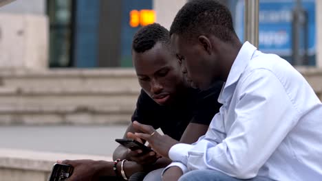 two-young-black-african-using-smartphone-sitting-in-the-city