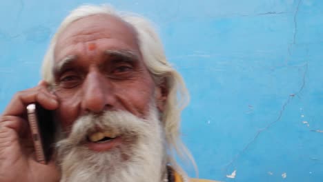 Tilt-up-closeup-of-a-bearded-Hindu-priest-wearing-traditional-saffron-clothes-on-a-call-in-Pushkar,-Rajasthan