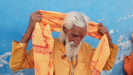 Indian-sadhu-saffron-holy-clothes-putting-on-a-turban-against-a-blue-wall