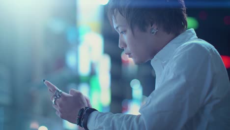 Portrait-of-the-Handsome-Alternative-Japanese-Boy-Using-Smartphone.-In-the-Background-Big-City-Advertising-Billboards-Lights-Glow-in-the-Night.