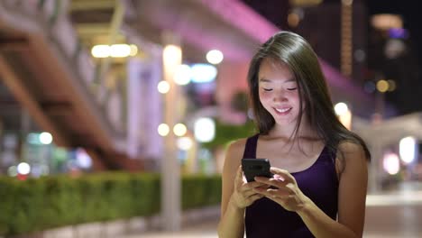 Hermosa-mujer-asiática-al-aire-libre-en-la-noche-con-teléfono-móvil