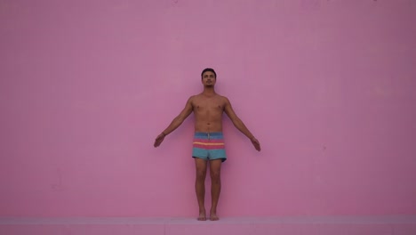 Mixed-race-hispanic-young-man-with-naked-torso-practicing-yoga-fitness-exercise-on-pink-background.-Sport,-meditation-and-lifestyle-concept.-Peaceful-Meditation-for-good-health