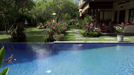 Vista-de-un-jardín-tropical-con-la-piscina-y-las-montañas-sobre-el-fondo-del-cielo-azul-en-un-día-soleado,-Bali,-Indonesia